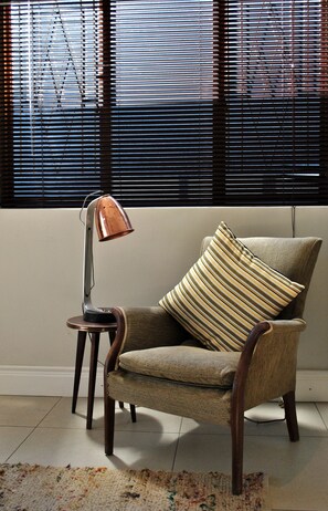 A chair with a striped pillow, a floor lamp, and a window with blinds.