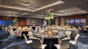 Un salón de banquetes con mesas redondas dispuestas para comer, sillas blancas y centros de mesa florales.