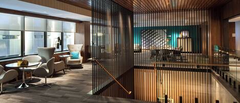 A modern interior with a wooden ceiling, a staircase, and a seating area with chairs and tables.
