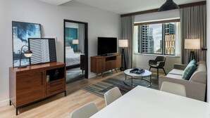 A modern hotel room with a bed, TV, seating area, and large windows offering city views. - Le Meridien Houston Downtown (Houston)