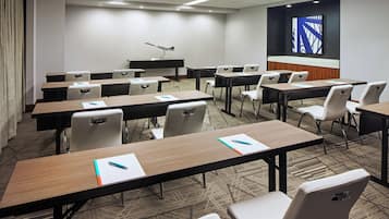 A conference room with multiple tables and chairs, a podium, and a large screen on the wall.