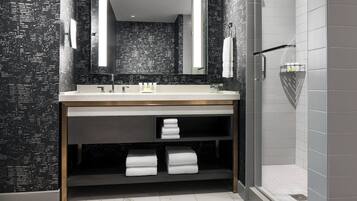 A modern bathroom with a dark patterned wall, a large mirror, a sink with a towel rack, and a shower area.