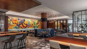 Um restaurante moderno com um mural colorido, uma coluna de madeira central e uma combinação de áreas de bar e refeições.