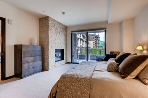 A bedroom with a bed, a stone wall, a television, and a balcony with a view of buildings.
