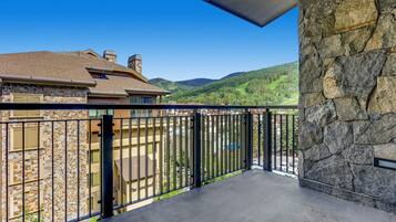 A balcony with a stone wall and metal railing, overlooking a valley with houses and greenery.