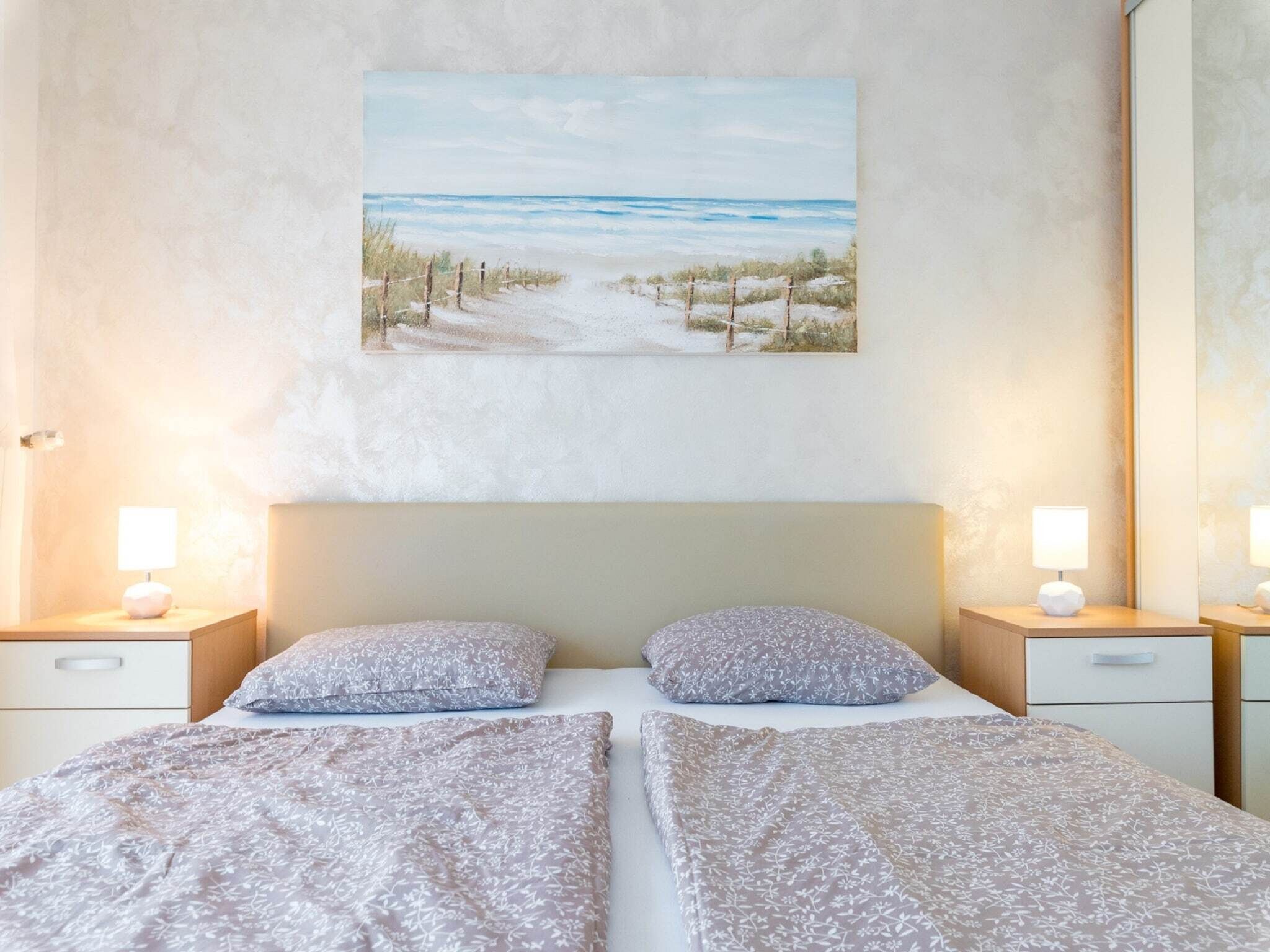 Een slaapkamer met twee bedden, een strandafbeelding aan de muur en bedlampen.