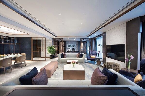 A modern living room with a sofa set, coffee table, and a TV. There is a dining area with chairs and a table. - Crowne Plaza Shanghai Pujiang by IHG (Shanghai)
