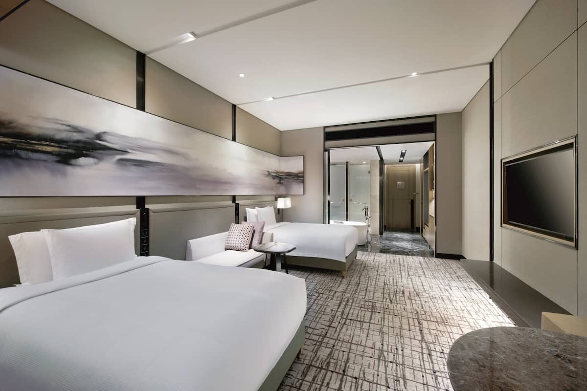 Ein modernes Hotelzimmer mit zwei Betten, einer Sitzecke, einem Fernseher und einem großen, abstrakten Gemälde an der Wand.
