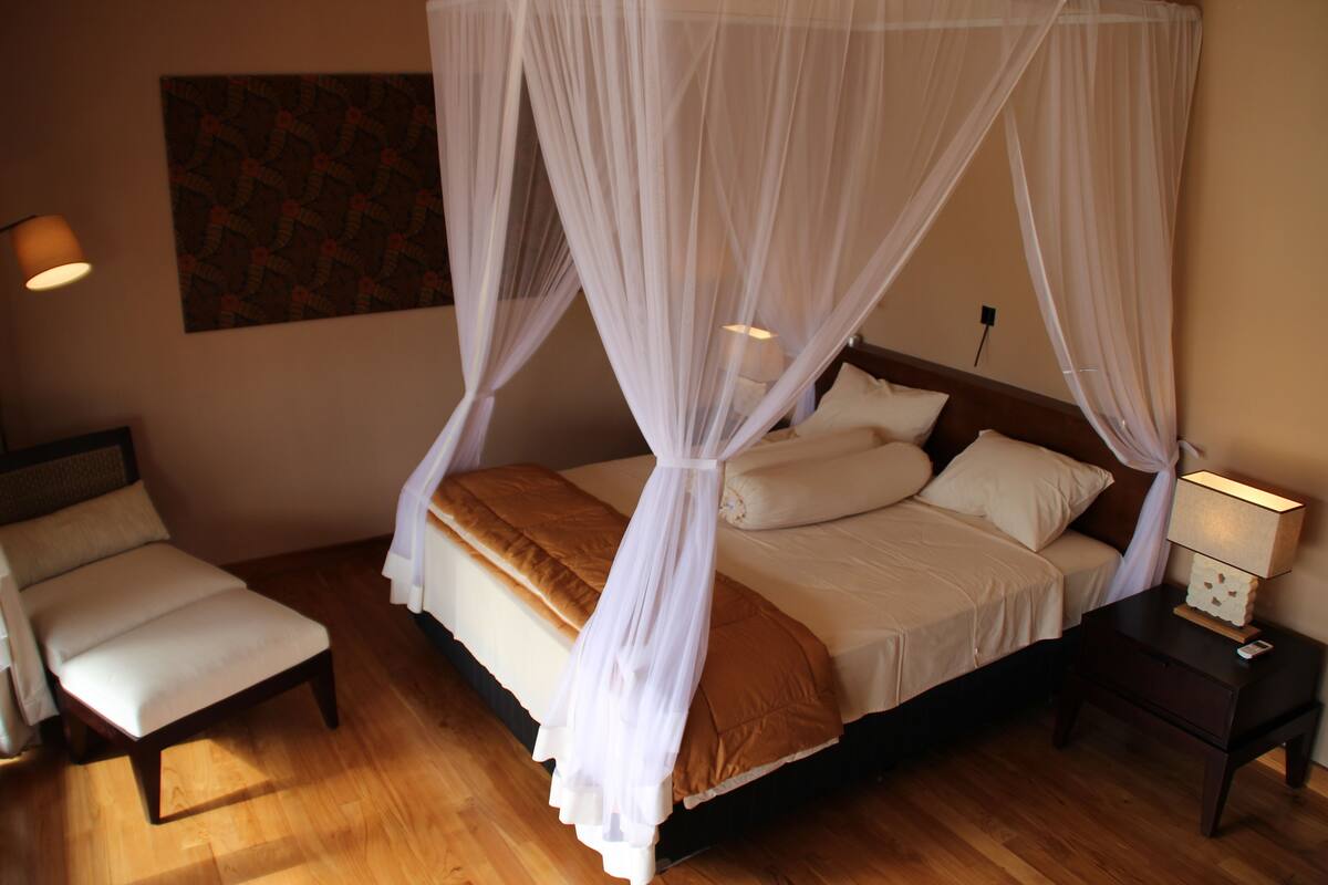 A bedroom with a four-poster bed, a bedside table with a lamp, and a chair.