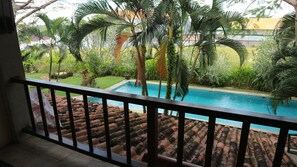 A pool surrounded by palm trees and greenery, viewed from a balcony with a tiled floor.