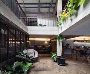 A spacious indoor area with a mezzanine level, potted plants, and a check-in/out sign. - Thunder Bird Hostel (Chiang Mai)