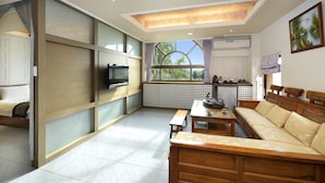 A modern living room with a sofa, a coffee table, and a TV. There is a window with curtains and a view of greenery outside. - Jinsa Lakeside View Hotel (Jinsha)