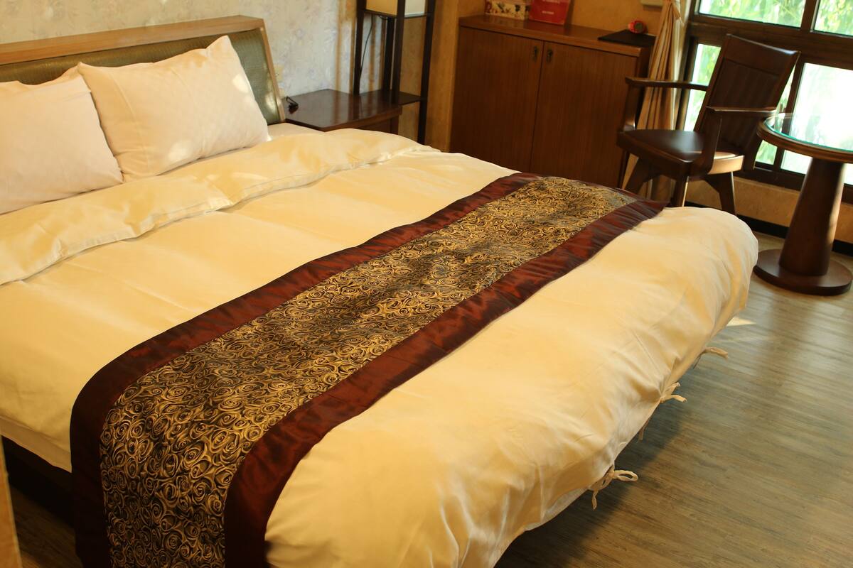 A neatly made bed with a patterned bedspread, a wooden headboard, and a nightstand with a lamp.