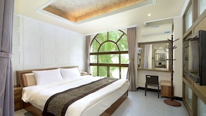A spacious bedroom with a large bed, a wooden nightstand, a chair, and a coat rack. - Jinsa Lakeside View Hotel (Jinsha)