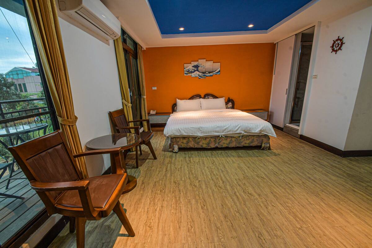 A hotel room with a bed, a chair, a table, and a balcony with a view of the outside.