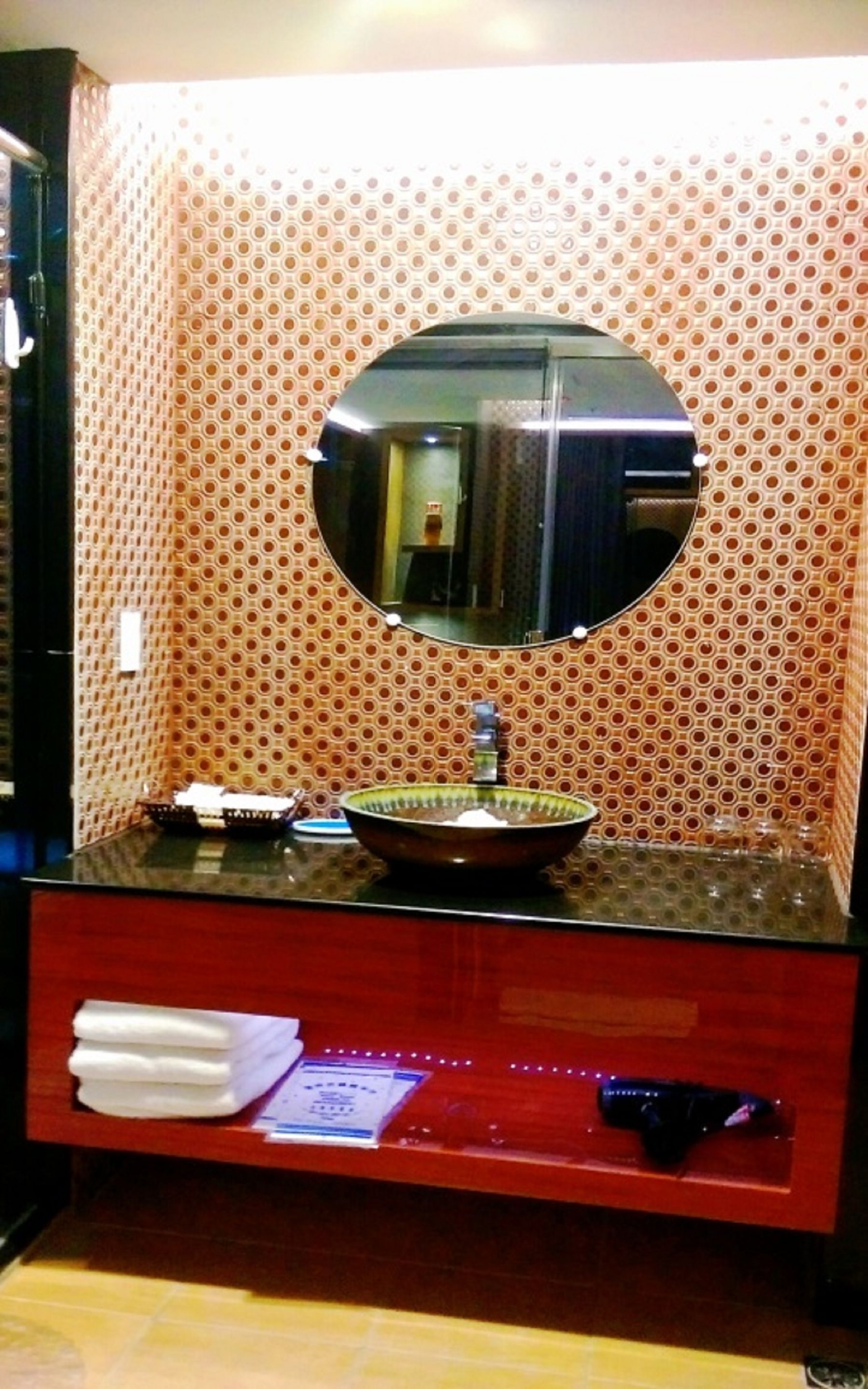 A bathroom with a round mirror, a bowl sink, and a vanity with a red countertop.