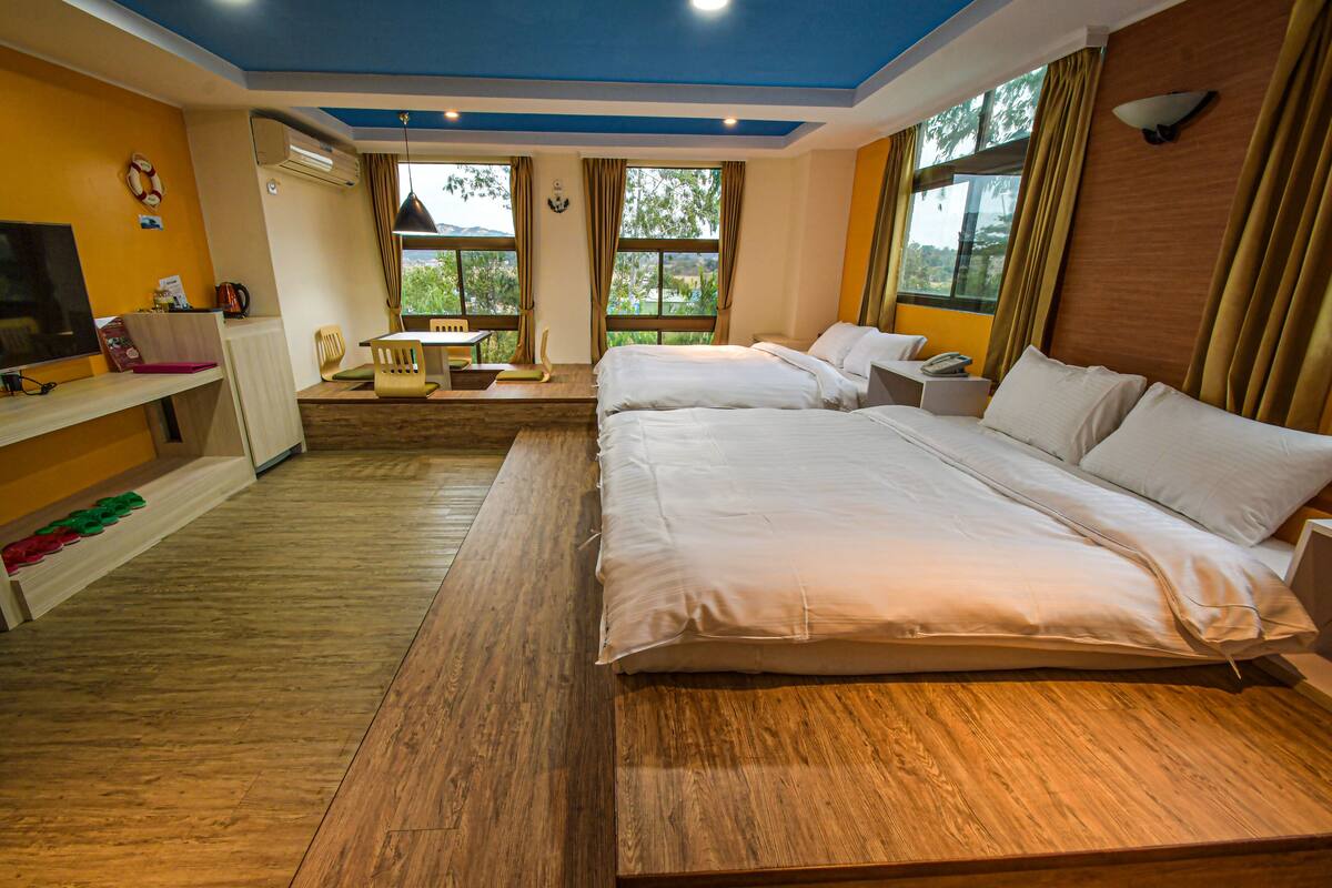A hotel room with two beds, a desk with a chair, a TV, and a view of the outdoors.