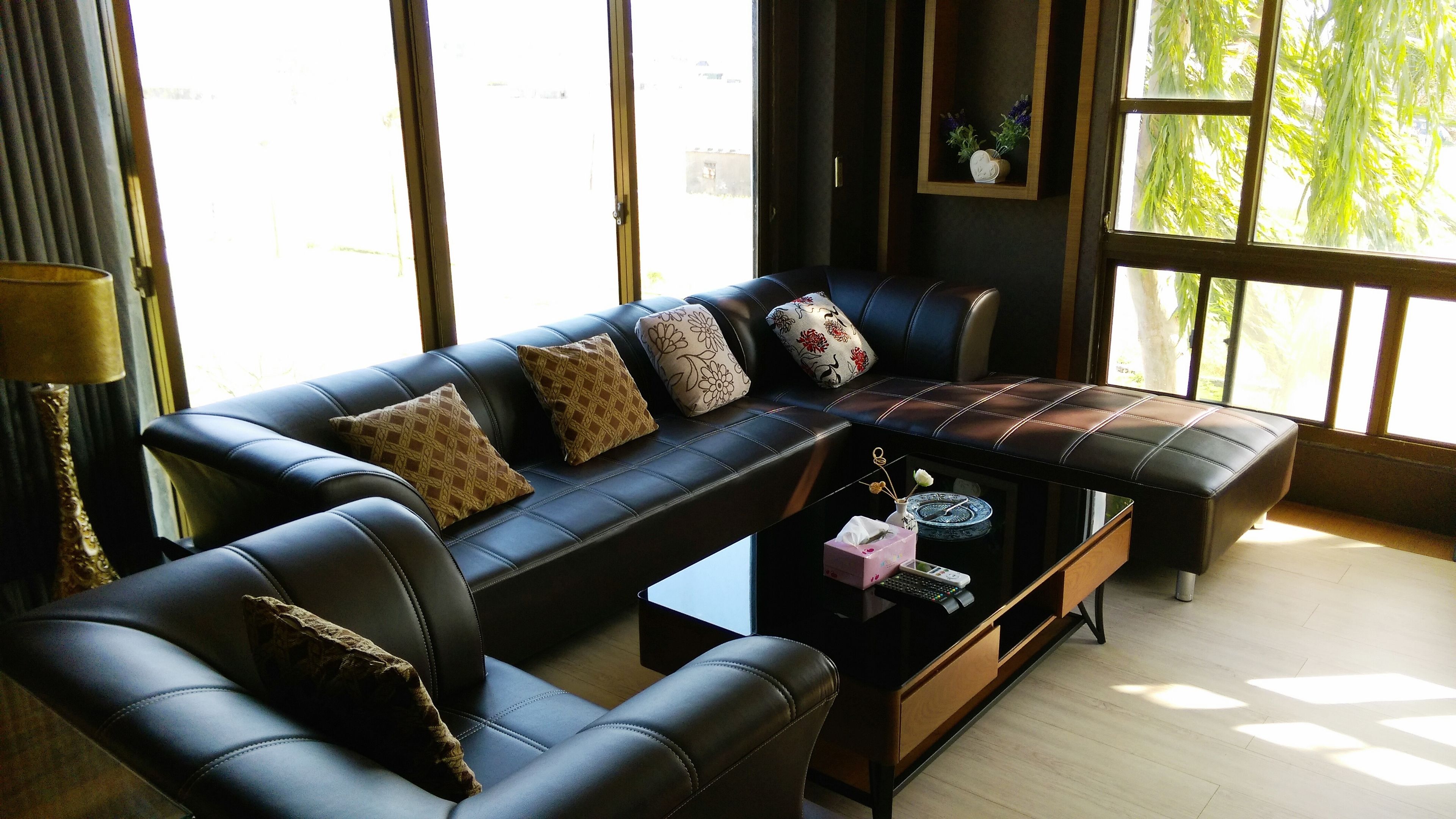 Uma sala de estar moderna com um sofá de couro preto, uma mesa de centro e uma janela grande.