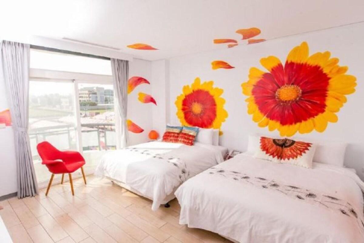 A hotel room with two beds, a red chair, and large floral wall art.