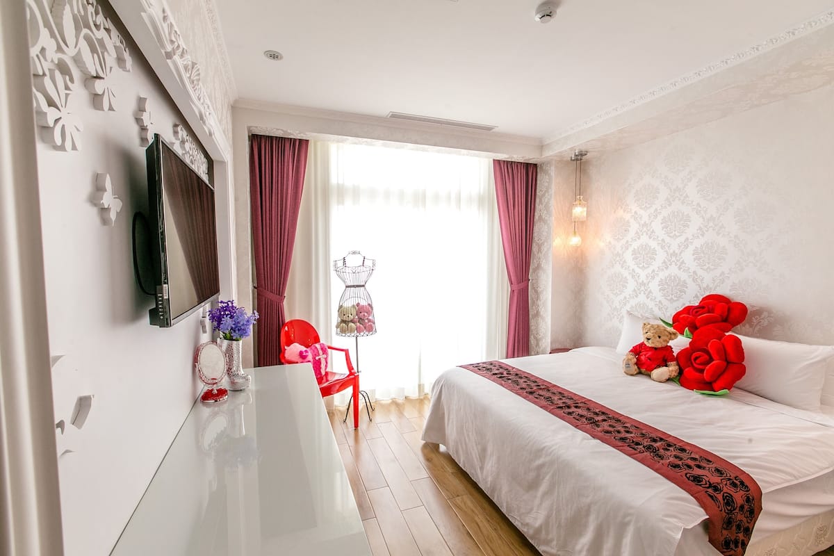 A hotel room with a large bed, a desk, a chair, and a window with curtains.