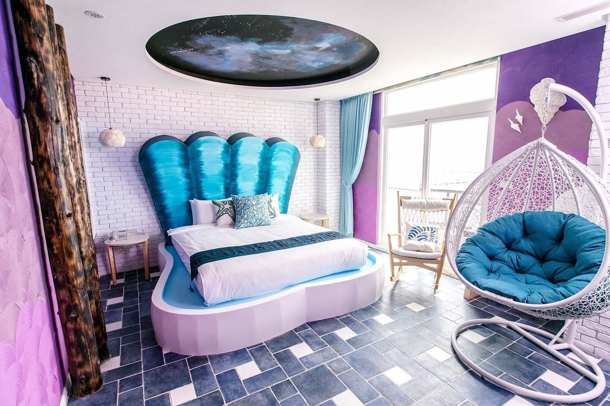A modern bedroom with a unique curved bed, a hanging chair, and a large window.