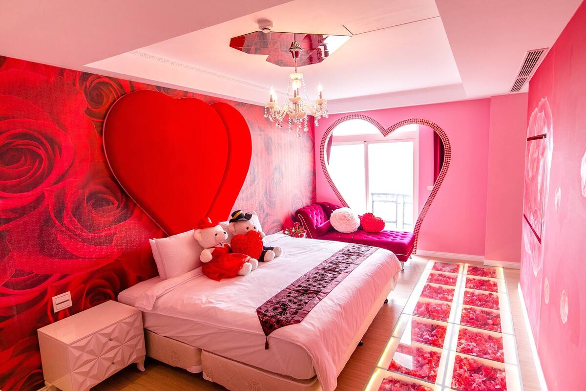 A pink-themed bedroom with a large bed, heart-shaped wall decor, and a chandelier.