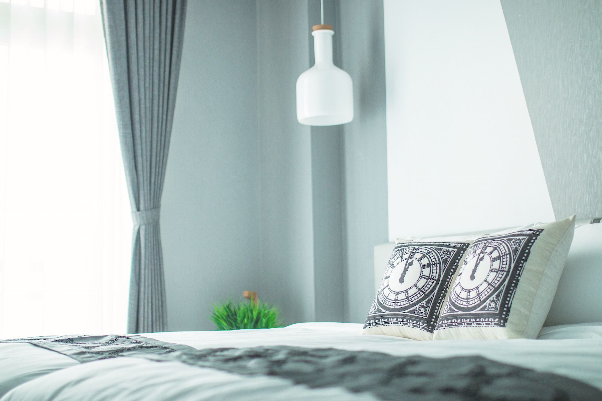 A bedroom with a bed, a hanging light fixture, and a small plant.