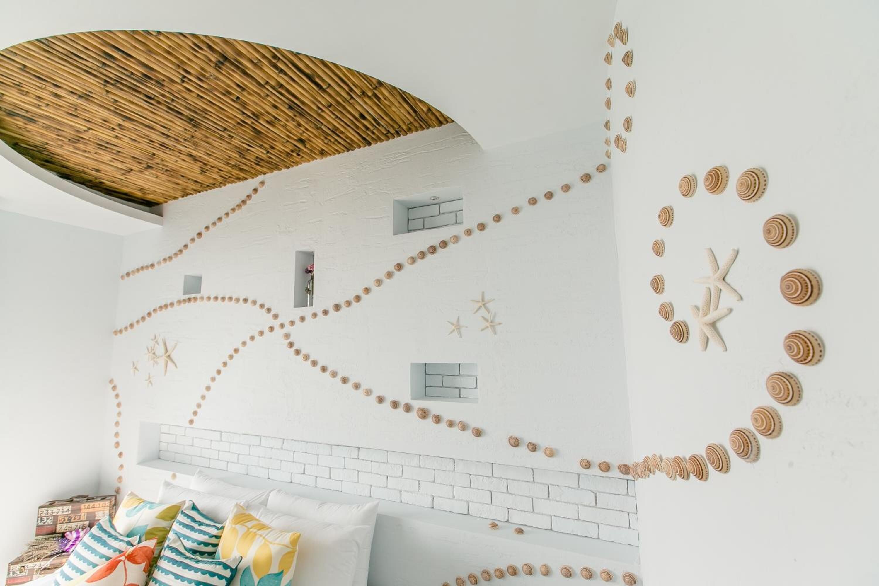 A room with a white brick wall, decorative starfish and seashells, and a woven ceiling.