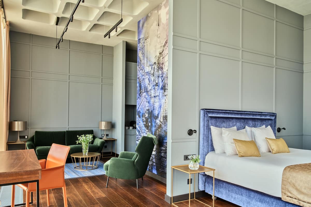 Een moderne hotelkamer met een groot bed, een groene fauteuil, een houten tafeltje en een muurschildering van een stadsgezicht.