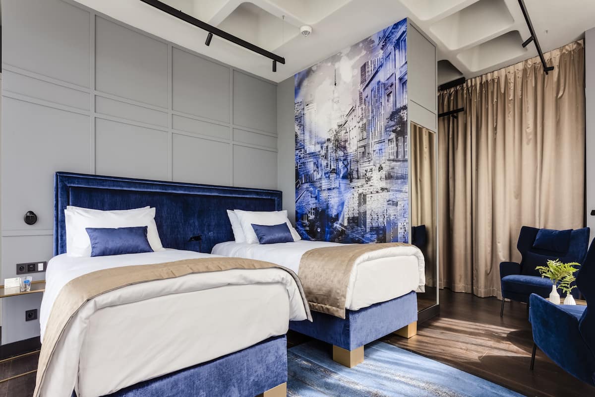 Een moderne hotelkamer met twee bedden, een grote stadsmuur, een blauwe fauteuil en een houten vloer.