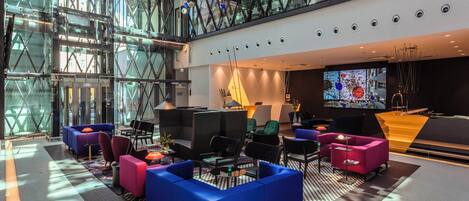 A modern lobby with a glass ceiling, seating areas, and a large screen.