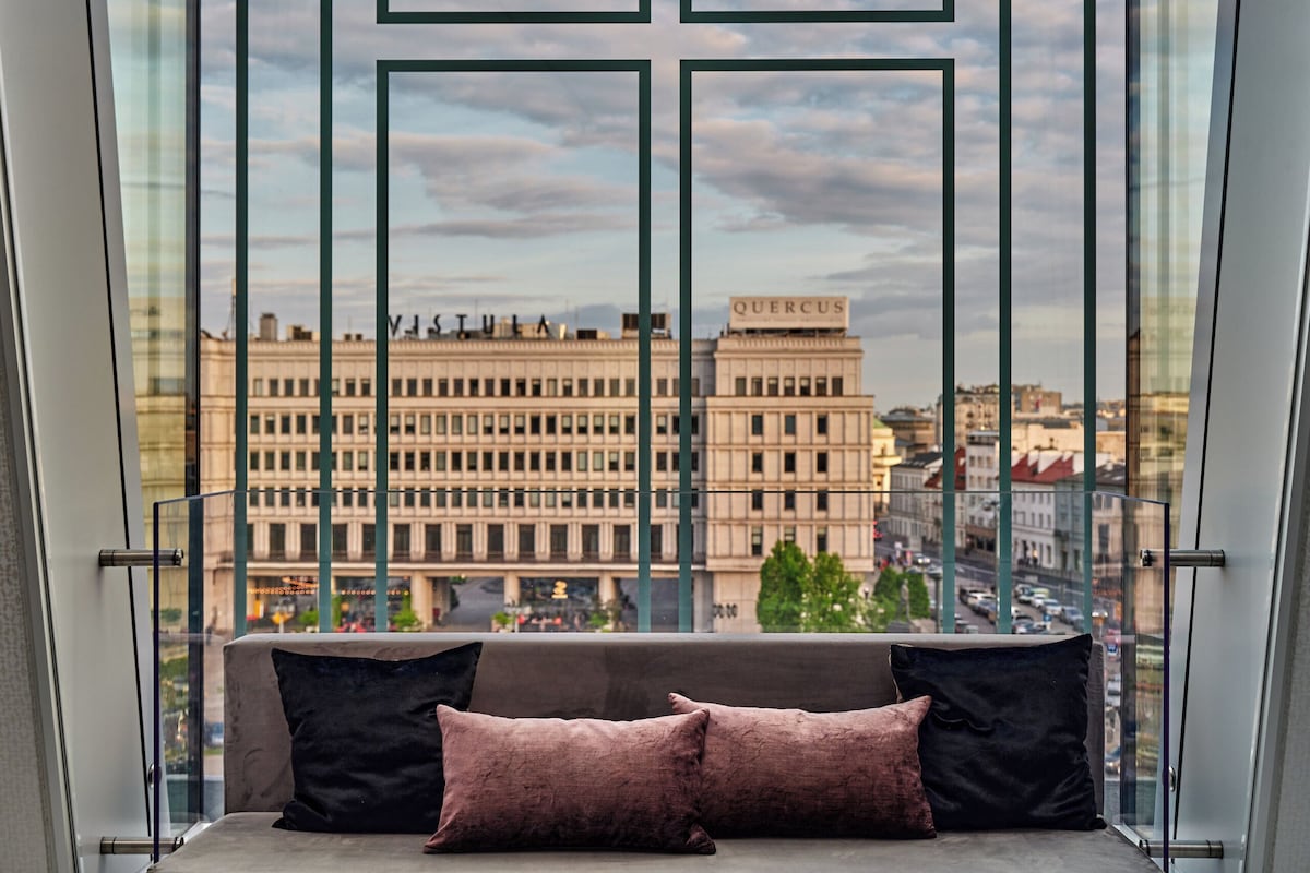 Ein Balkon mit Glastrennwand, einer gepolsterten Bank und einem dekorativen Metallornament.