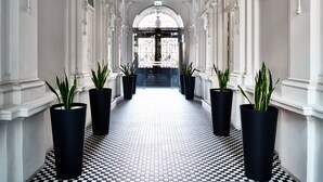 Un couloir doté d’un sol à carreaux noirs et blancs, de colonnes blanches et de jardinières noires contenant des plantes vertes.