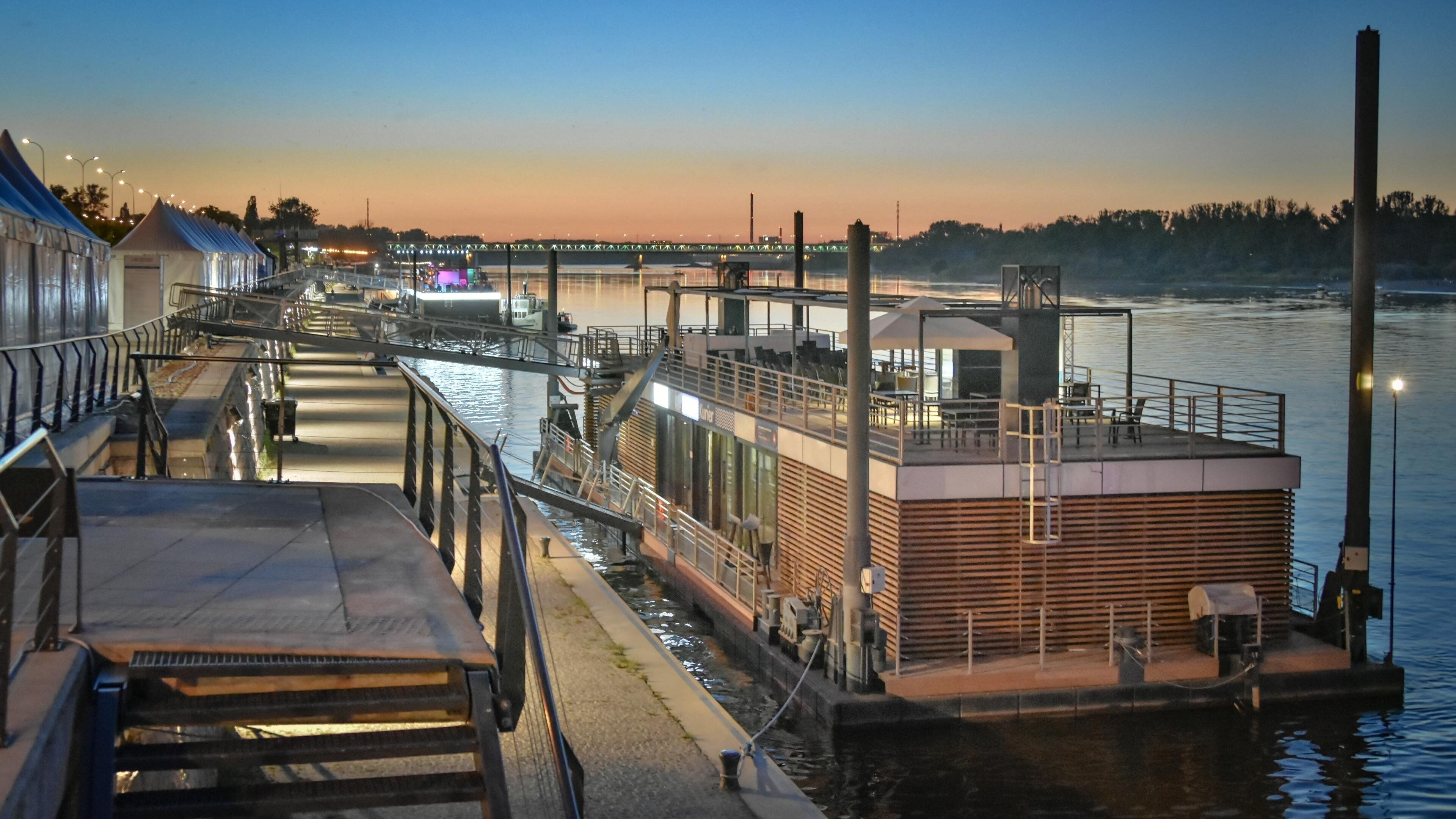 A waterfront dock with a boat, a covered walkway, and a building with a flat roof.