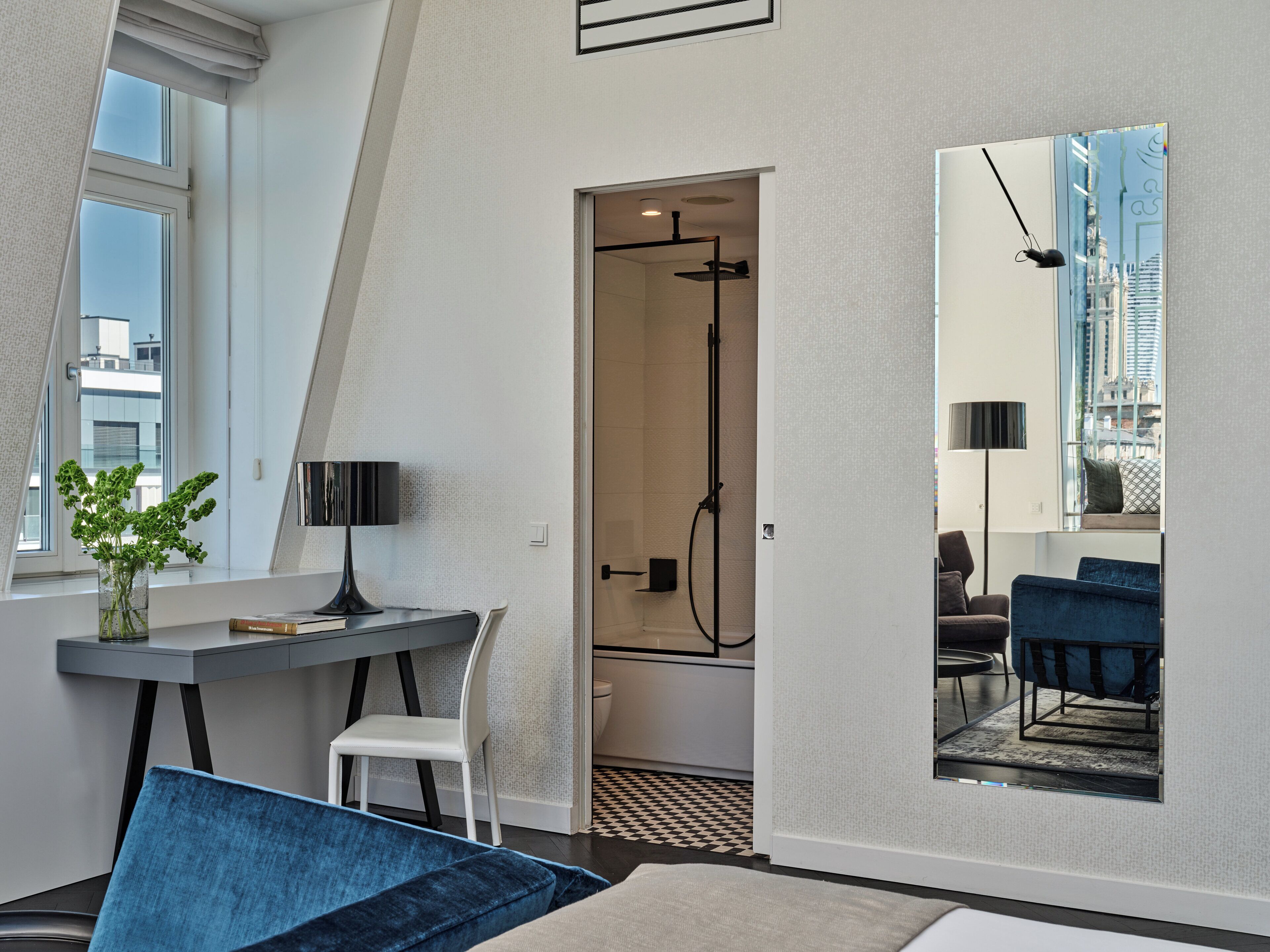 A modern hotel room with a dining area, a shower, and a large mirror reflecting the cityscape.
