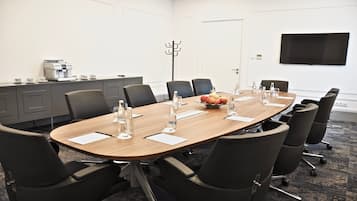 Een vergaderruimte met een lange tafel, stoelen, een koffieapparaat en een schaal fruit.