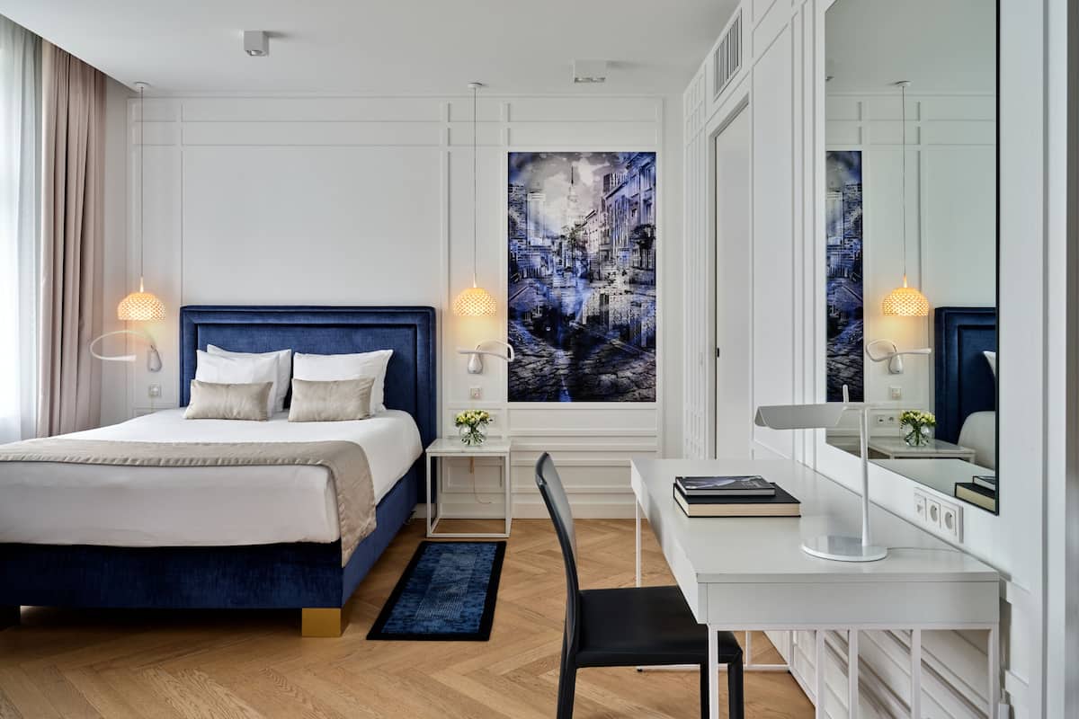 Een moderne hotelkamer met een groot bed, een bureau met een stoel, en een groot raam met uitzicht op de stad.