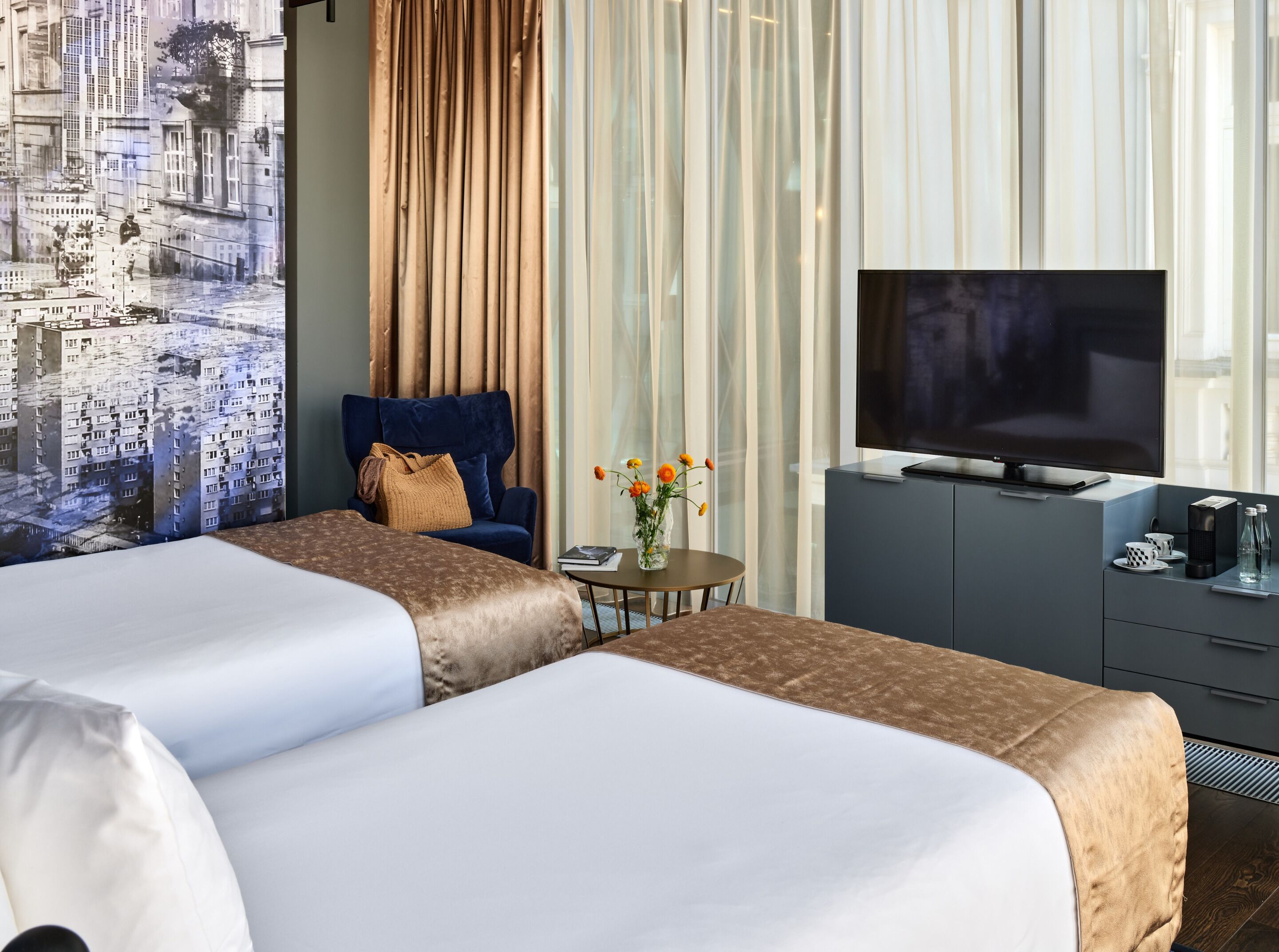 A hotel room with two beds, a TV, a small table with a vase of flowers, and a chair.