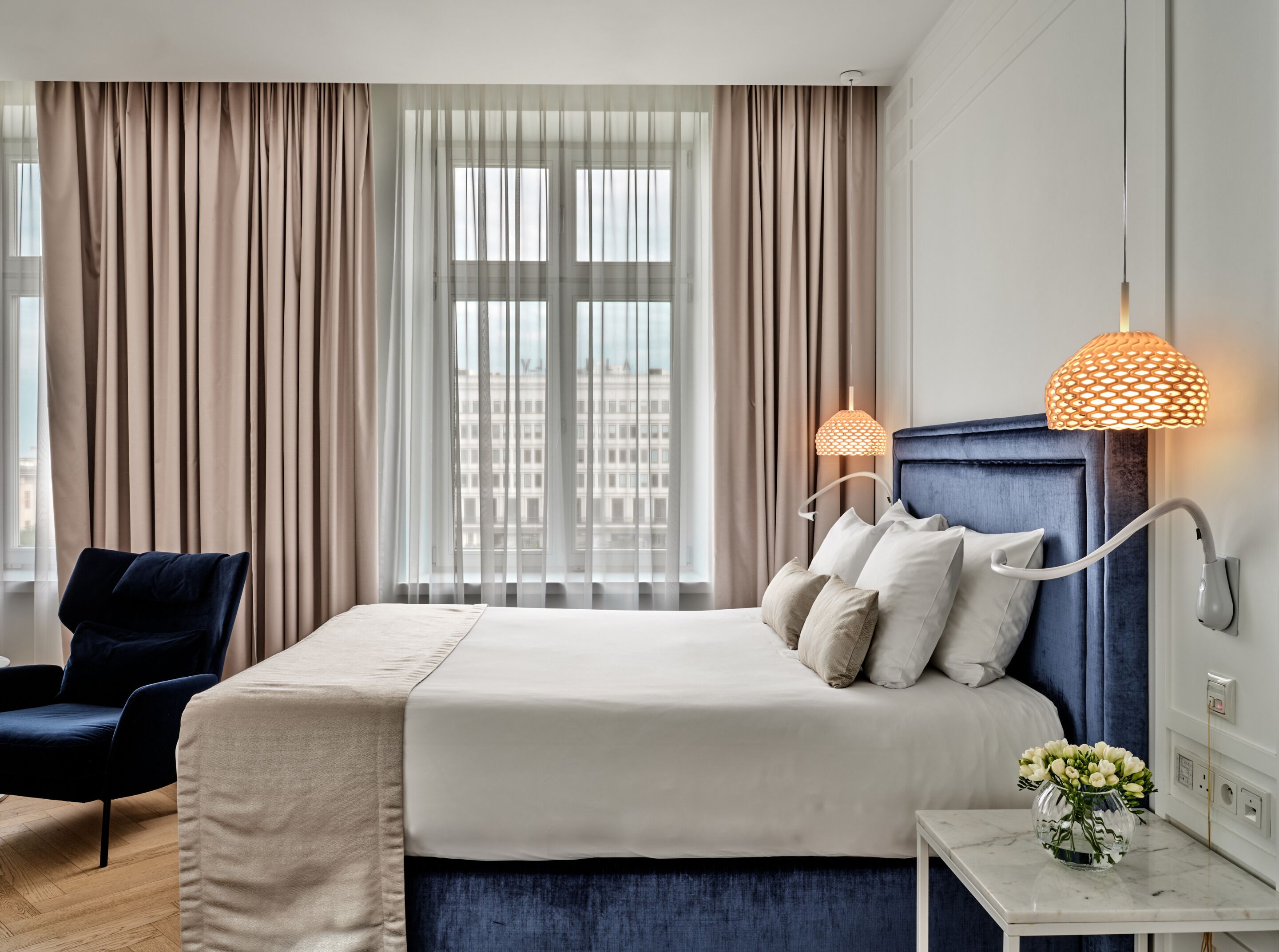 A hotel room with a large bed, a chair, a nightstand, and a window with curtains.
