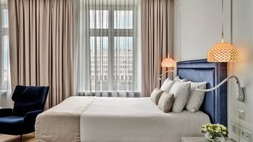 A hotel room with a large bed, a chair, a nightstand, and a window with curtains.