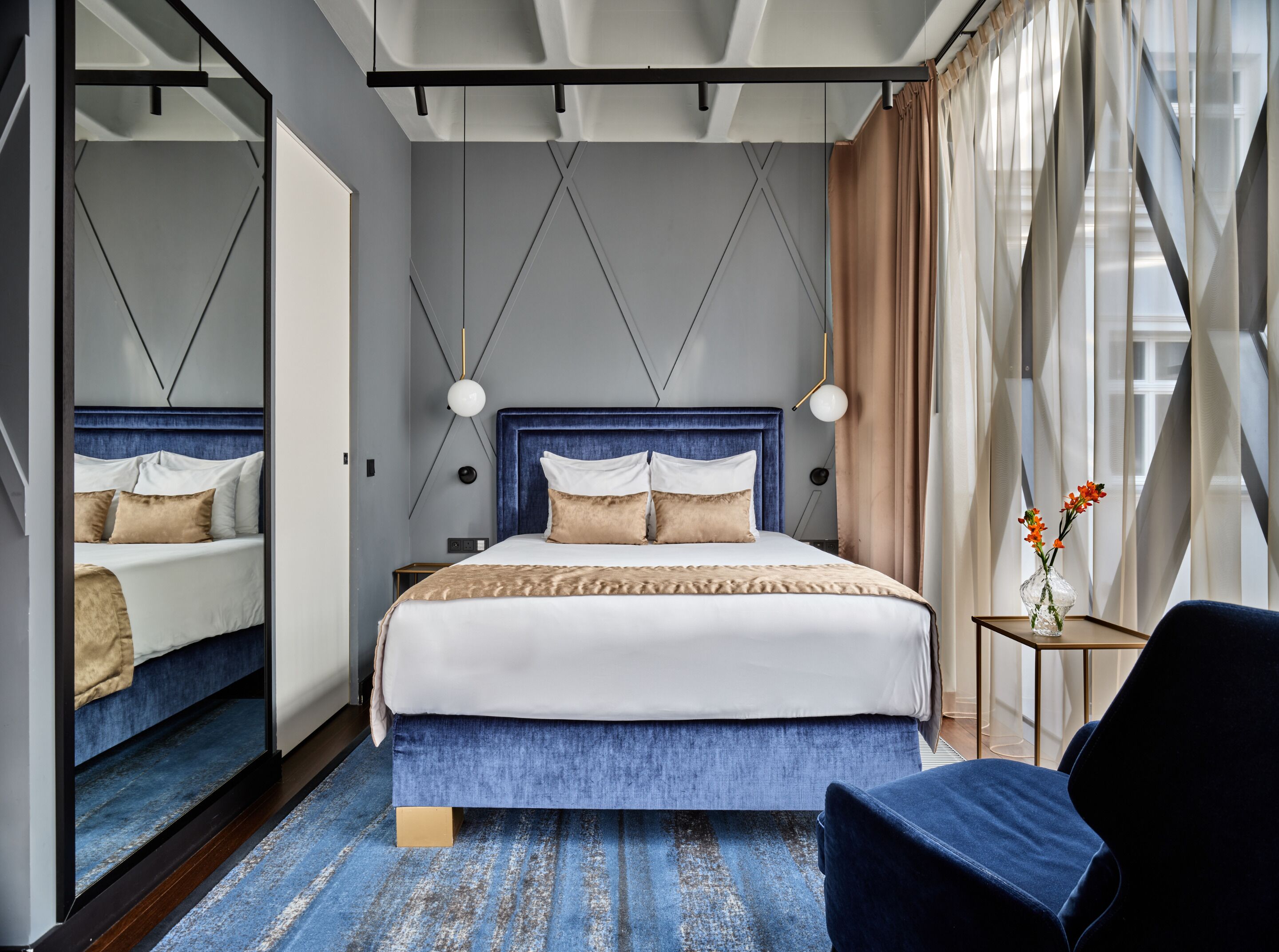A modern bedroom with a large bed, a bedside table, a chair, and a mirror.
