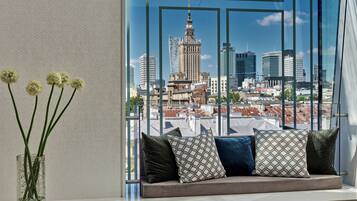 Un balcon avec vue sur la ville, un vase en verre rempli de fleurs et des coussins à motifs.
