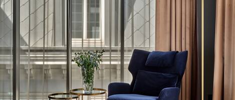 A modern living room with a blue armchair, a round floor lamp, and a glass vase with flowers on a small table.
