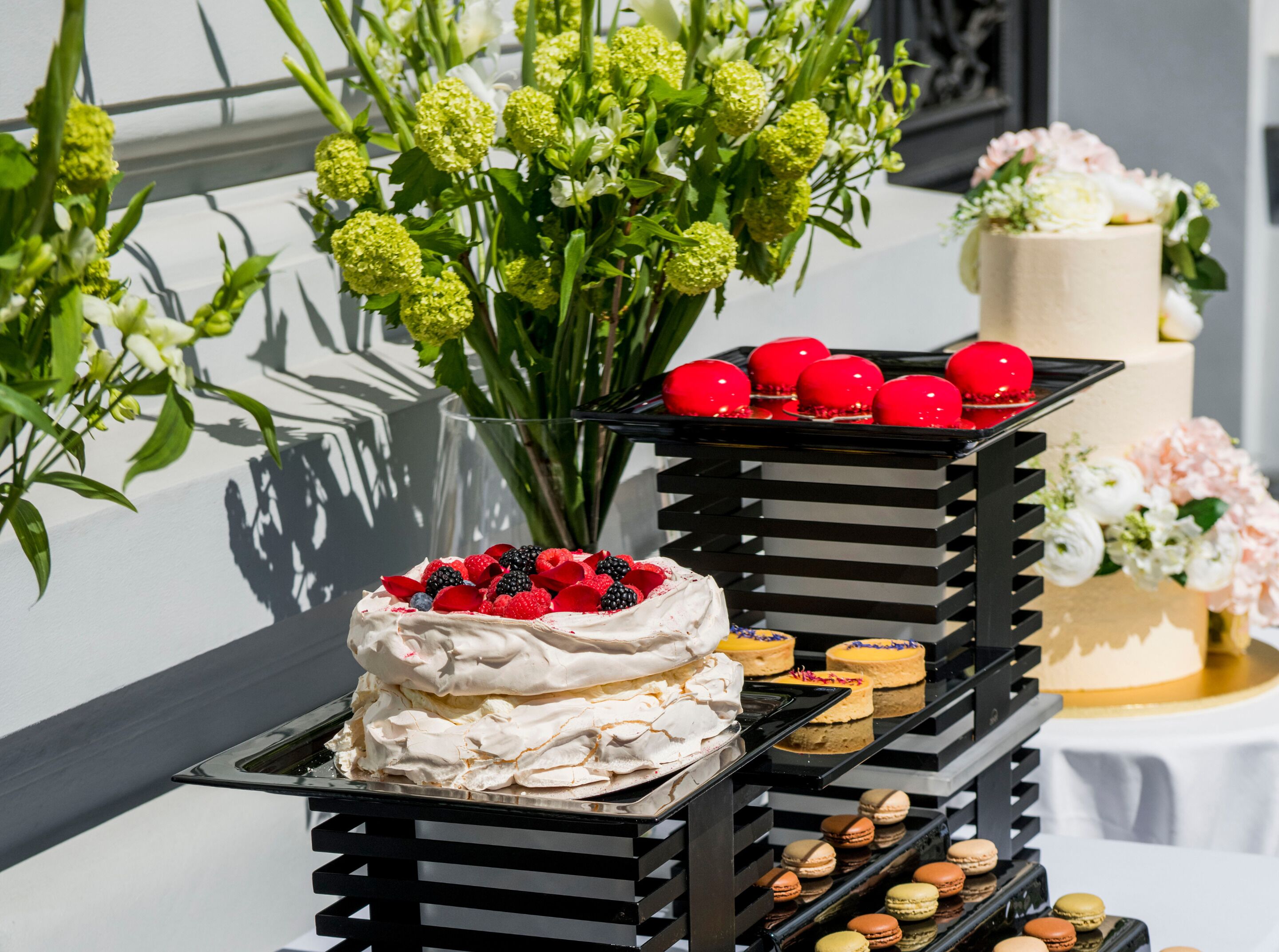 Una presentación de postres con pastel, macarons y un jarrón de flores.