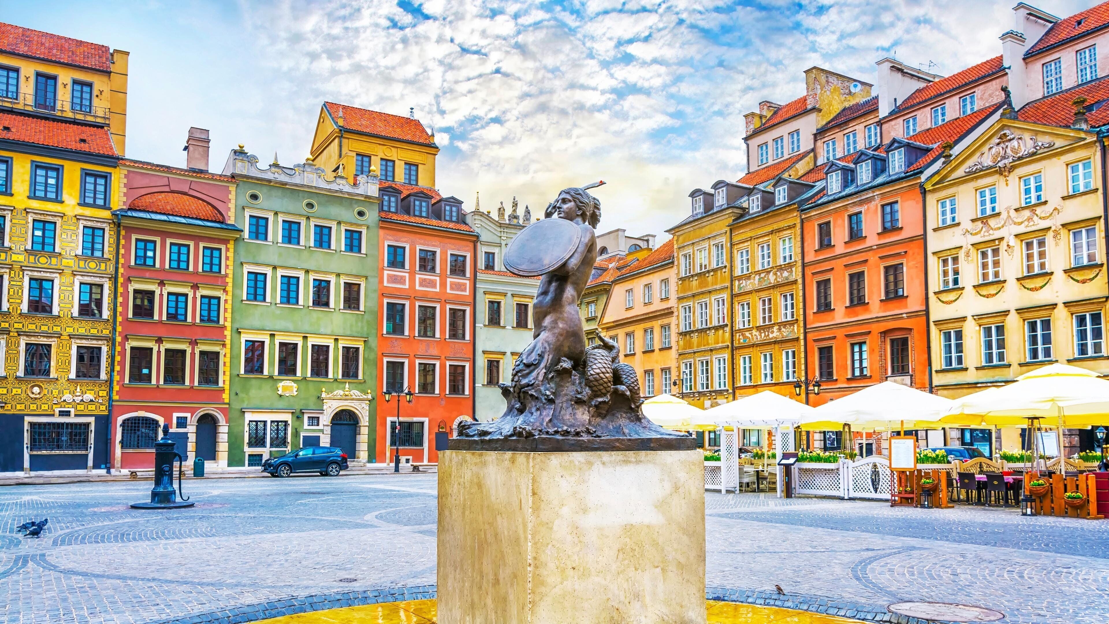 Una piazza con una statua al centro, circondata da edifici colorati con diversi stili architettonici.