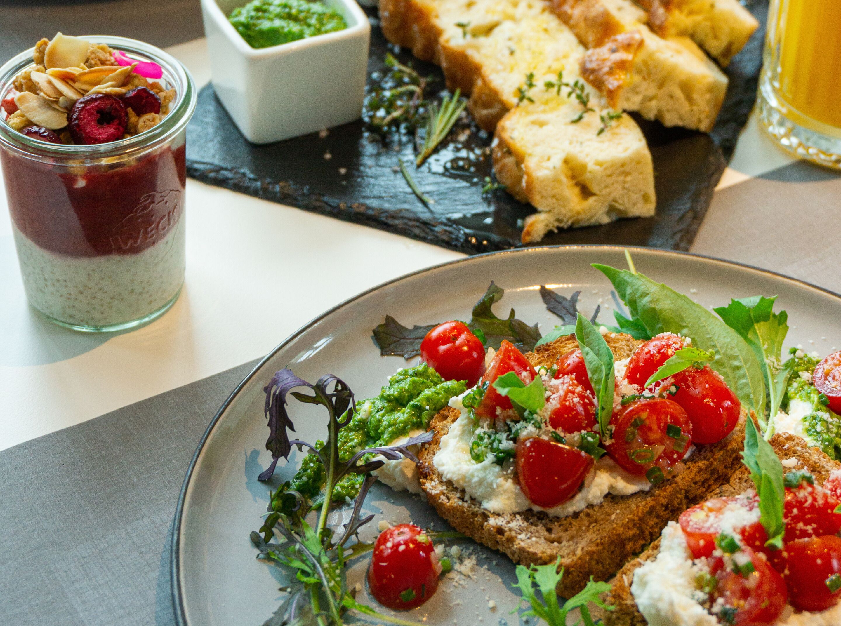 En tallerken med bruschetta overdækket med tomater, ost og grønt, et glas bærkompot og et glas øl på en skiferplade.