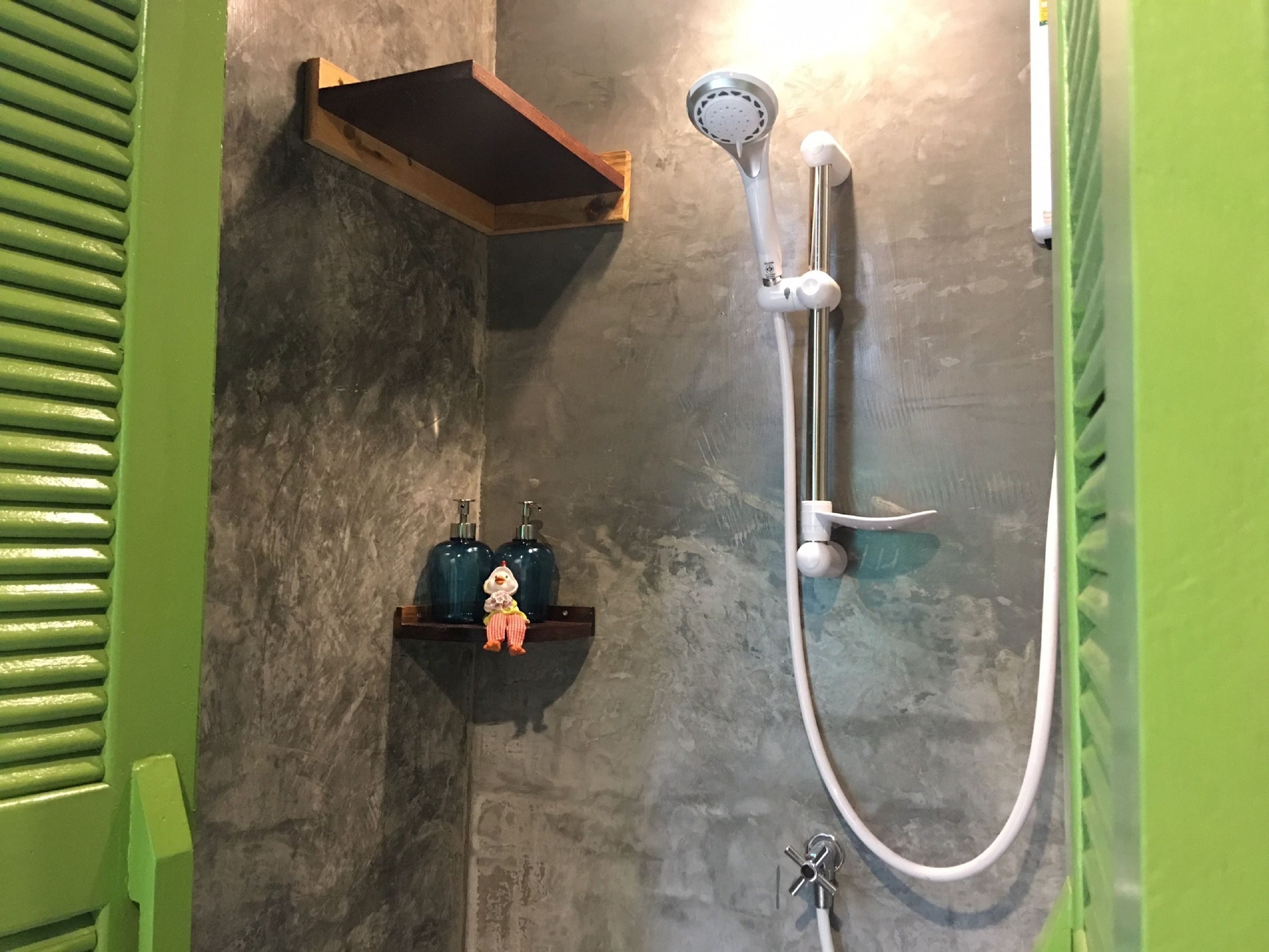 A shower area with a handheld showerhead, a wall-mounted faucet, and a shelf with toiletries.