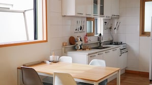 A compact kitchen with white cabinets, a wooden table, and a window. - Hongdae One House (Seoul)