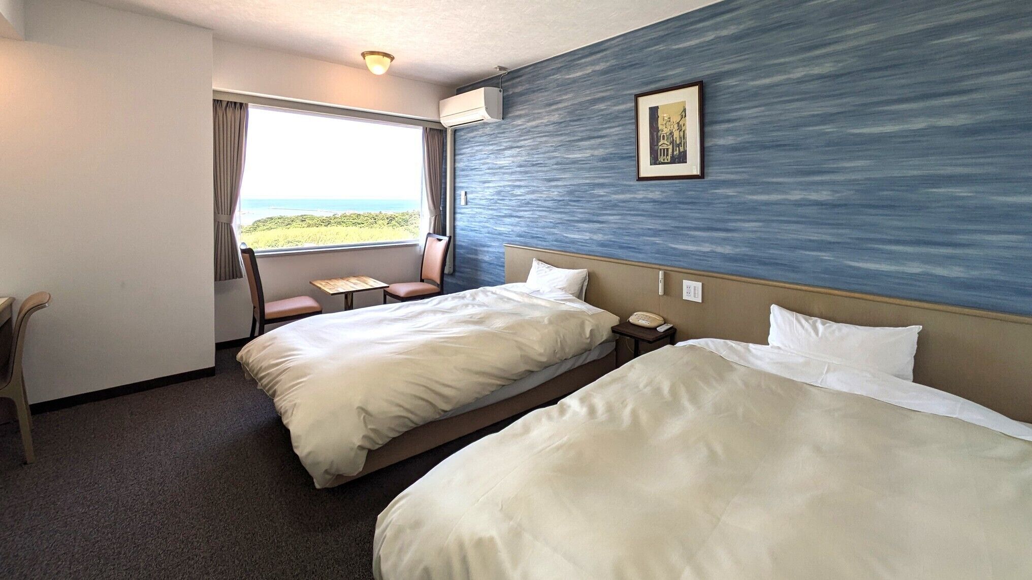 Ein Hotelzimmer mit zwei Betten, einem Sessel, einem kleinen Tisch, einem Telefon und einem Fenster mit Blick.