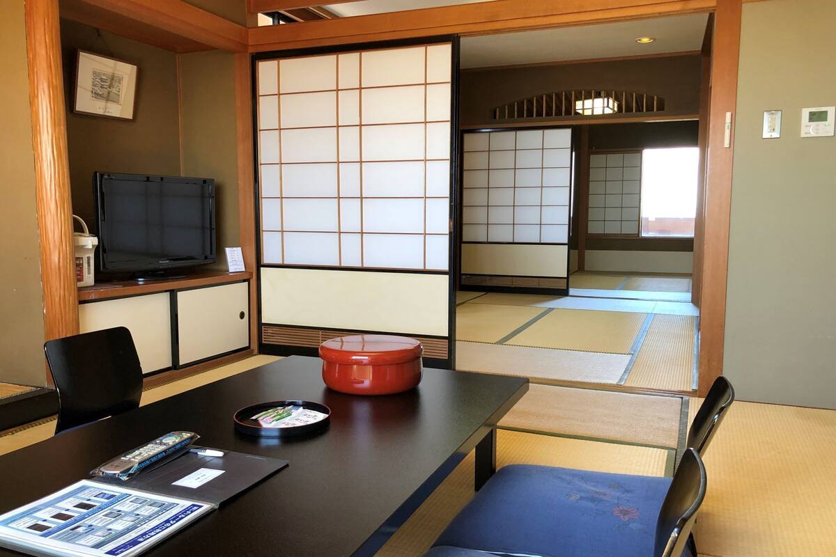 A traditional Japanese room with tatami flooring, a tatami mat table, a television, a red container, and a blue cushioned bench.